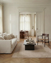 Modernes Wohnzimmer mit hellem Leinensofa, dunklem Holztisch und minimalistischer Ästhetik in neutralen Beige-Tönen.