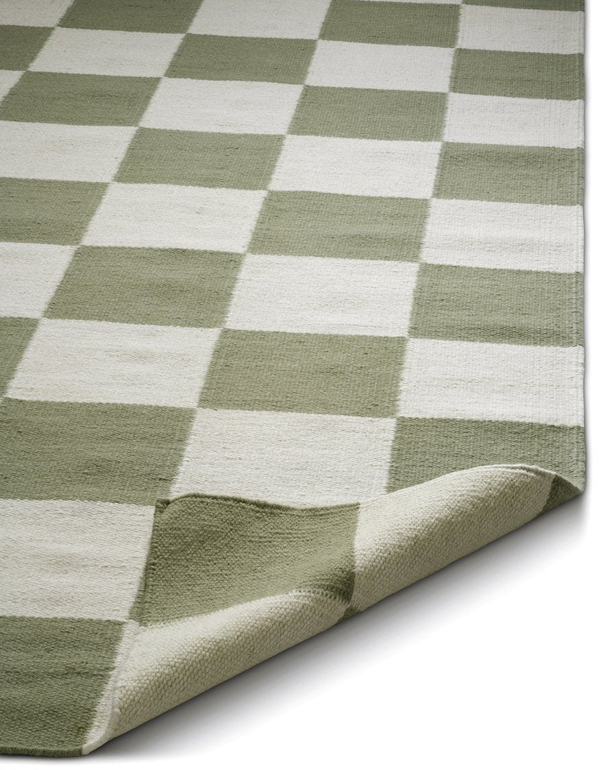 Teppich mit kariertem Muster in Salbeigrün und Creme, gewebte Textur mit umgeschlagener Ecke.