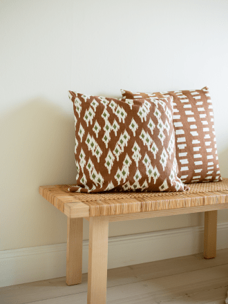 Cushion covers Ikat Diamond Terracotta and Ikat Block Terracotta in cotton, 50x50 cm, placed on a wooden bench with woven seat a