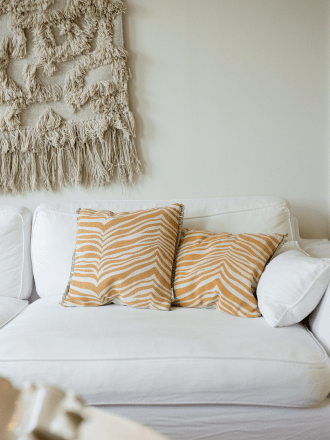 Kissen Zebra Gelb in den Größen 50x50 cm und 40x60 cm, aus Baumwolle mit Jutekante, auf einem weißen Sofa mit Wandteppich im Hin