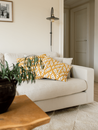 Kuddfodral Ikat Diamond Ockra och Ikat Block Ockra i bomull, 50x50 cm, placerade i en ljus soffa i vardagsrum med vägglampa och 