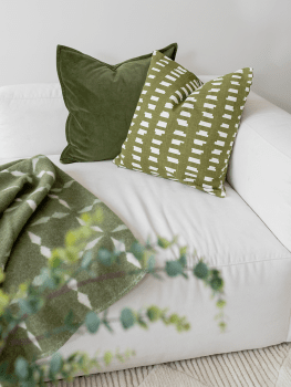 Kuddfodral Ikat Block Grön i bomull med grafiskt mönster, placerat på vit soffa tillsammans med grönt sammetfodral.