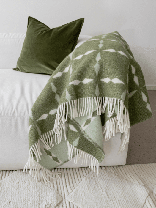 Kuddfodral Classic Velvet Skogsgrön i mjuk bomullssammet, placerat på vit soffa tillsammans med grön ullpläd Tile.